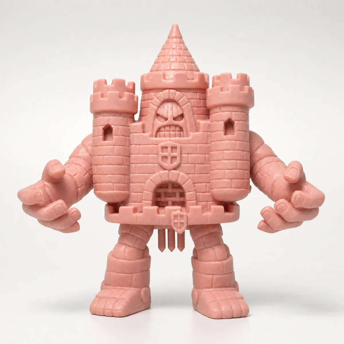 A pink toy figure whose torso is a castle with towers, a gate and a face in its keep, with arms and legs.