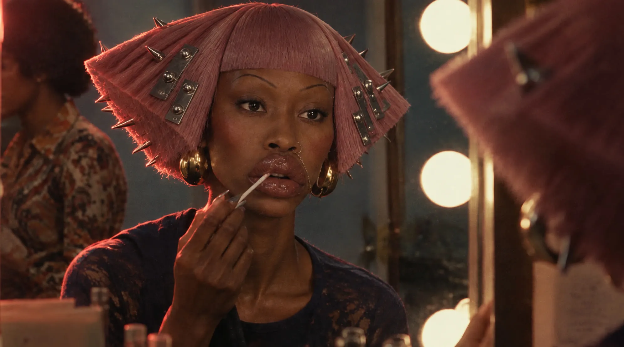 The same scene relit, a warm orange rim along the left side of the wig and her shoulder, the room behind her a shade darker.